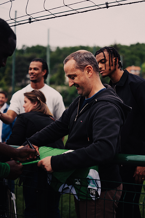 Discussion au bord du terrain entre partenaires et acteurs du club dans un cadre sportif extérieur.